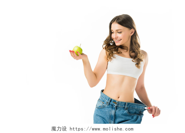 在白色背景下减肥成功的女人快乐苗条的年轻女子在大牛仔裤举行绿色苹果孤立在白色